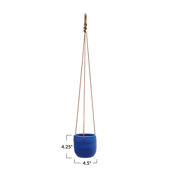 A blue stoneware planter with a matte latex finish, suspended by a leather rope hanger.