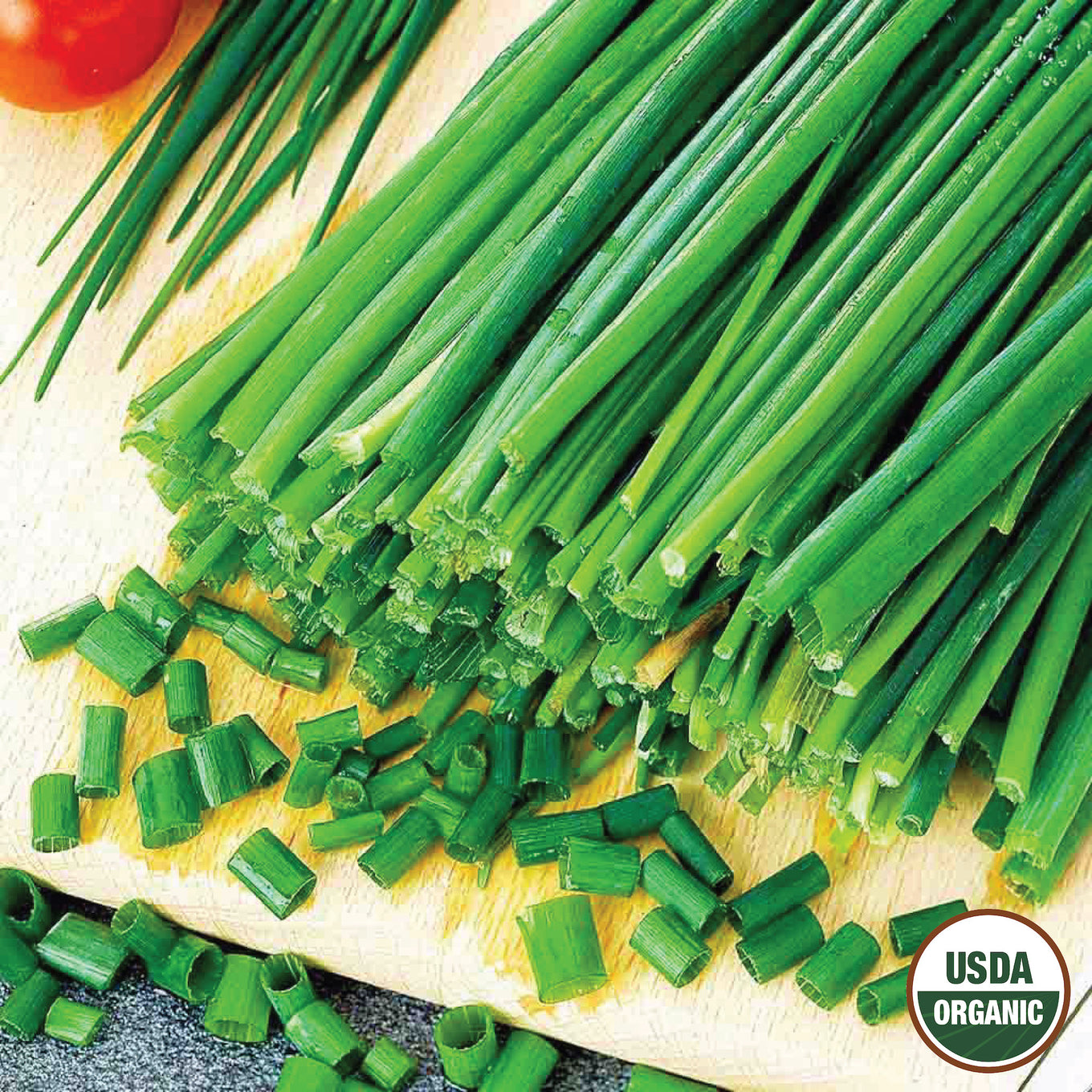 A bunch of fresh green chives with both whole stalks and chopped leaves displayed on a wooden surface, featuring a USDA Organic label.