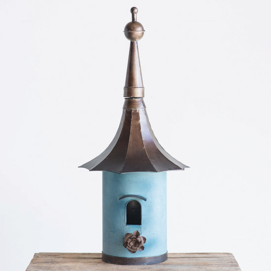 Decorative birdhouse with a blue body and bronze roof on a white background