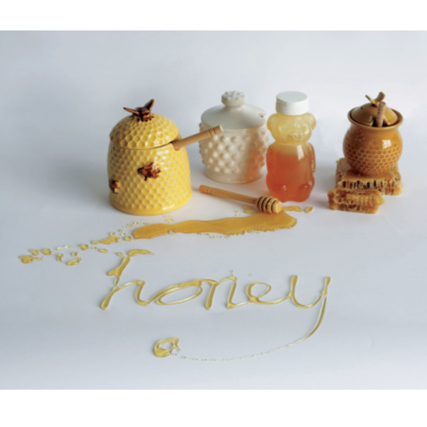 A stoneware honey jar with a yellow bee design, including a lid and a wooden honey dipper.