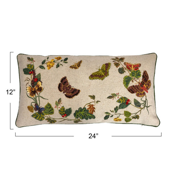 A rectangular cotton lumbar pillow with an embroidered butterfly and flower design on a beige mud cloth background, featuring green piping around the edges.