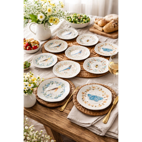Table setting with decorative plates featuring bird illustrations, surrounded by flowers and bread.