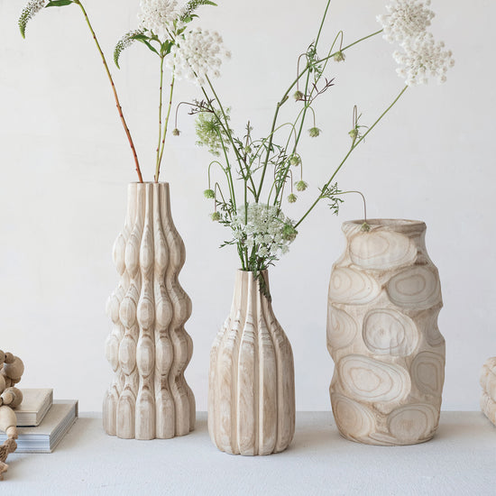 Three textured vases with floral arrangements on a light surface against a white background