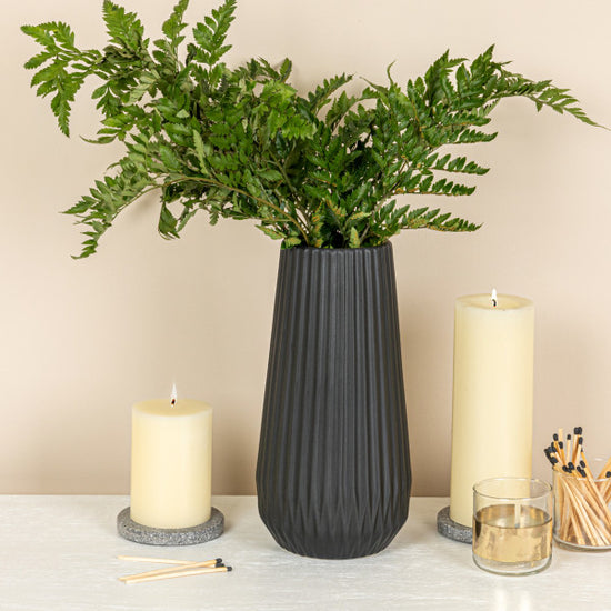 A tall black stoneware fluted vase with embossed lines, designed to hold flowers or foliage.