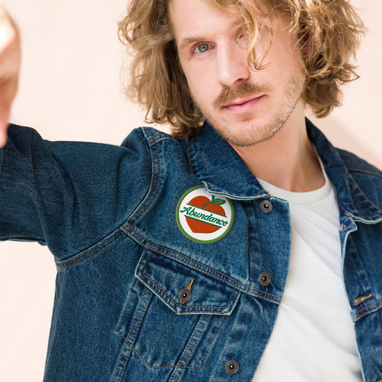 Man wearing a denim jacket with an 'Abundance' patch on a beige background