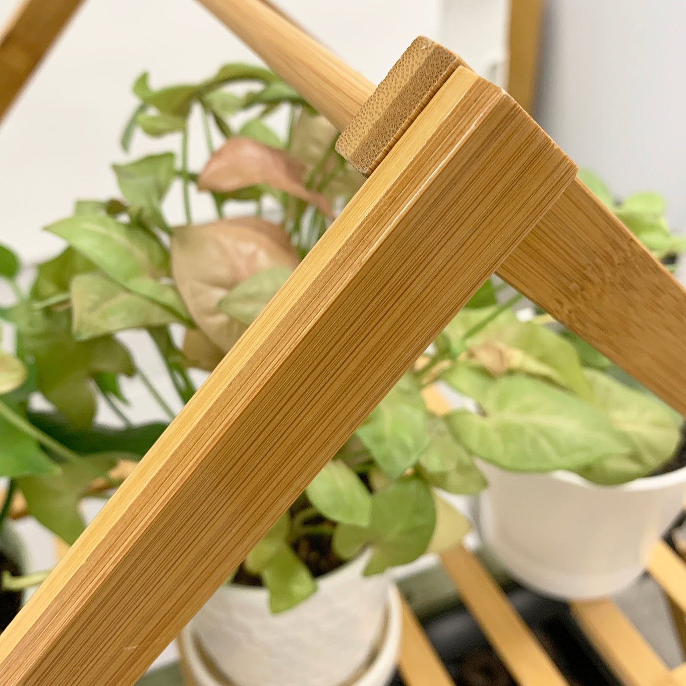A close-up of a bamboo indoor plant stand with multiple tiers, featuring wooden slats and supporting several potted plants.