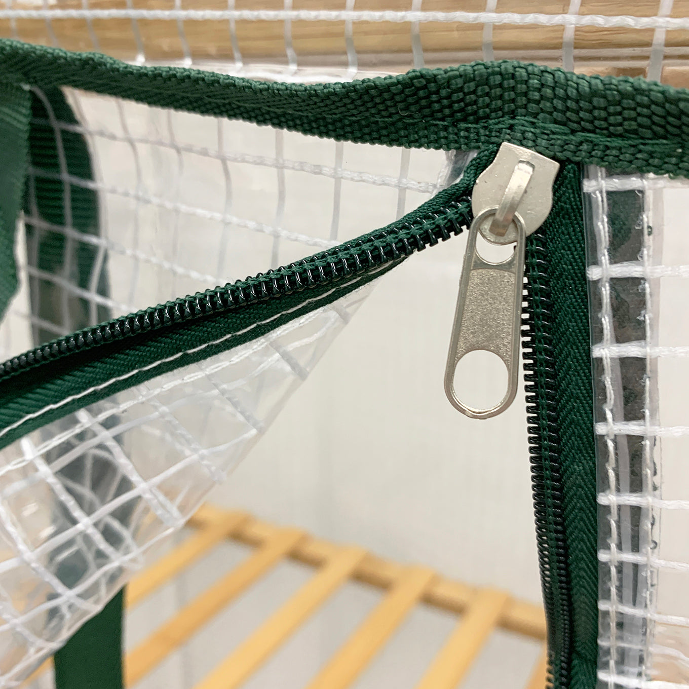 A clear plastic greenhouse cover with dark green edging, designed to fit on an indoor plant stand.