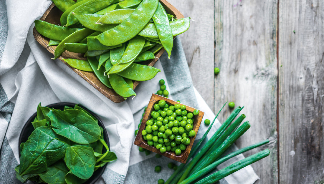 Peas, spinach, and onions assembled on a thin white cloth on a weathered wooden table