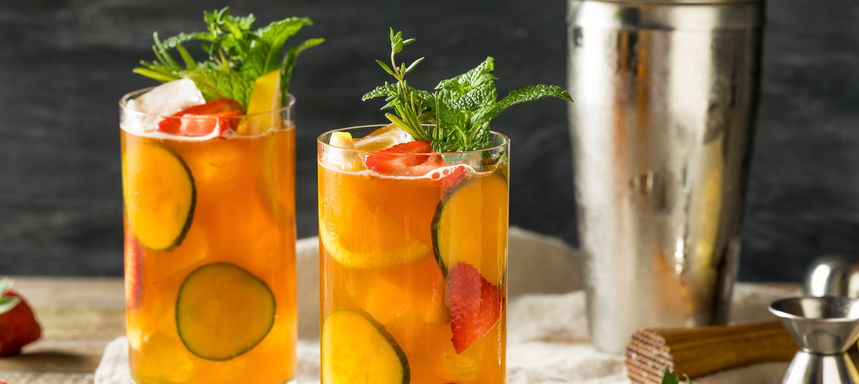 Two glasses of orange cocktails with fruit and mint garnishes on a wooden surface.