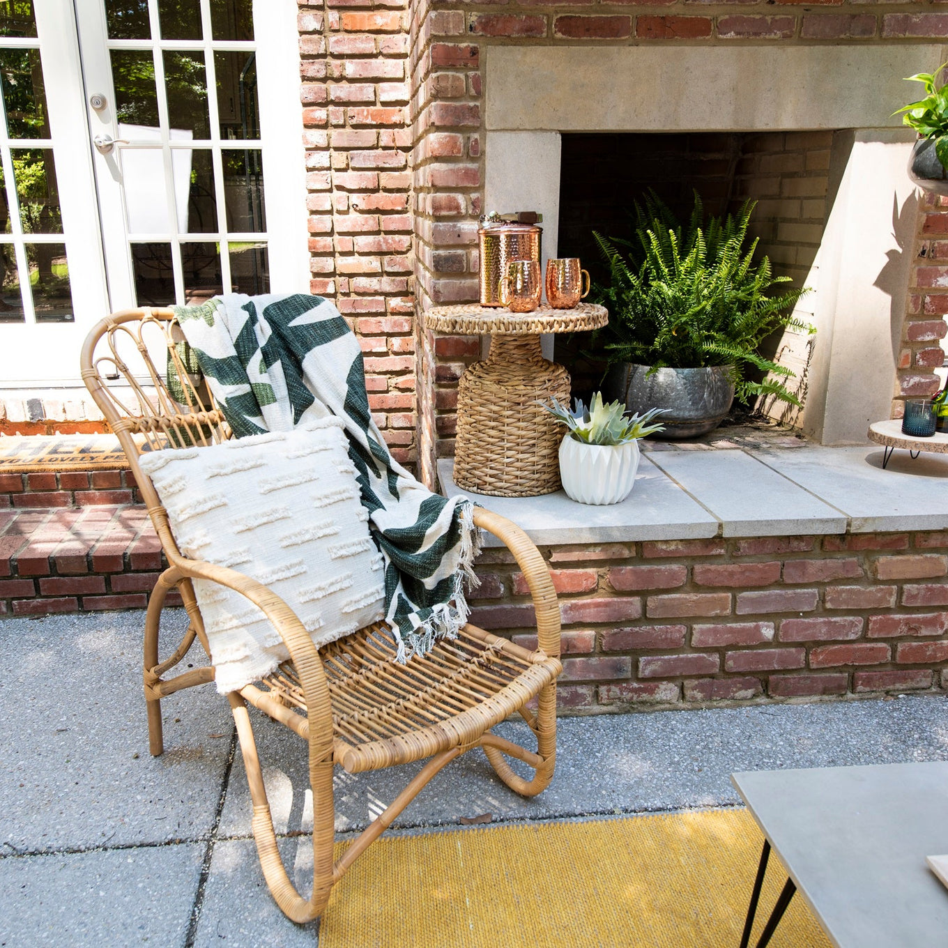 Outdoor patio with wicker chair, blanket, and fireplace area.