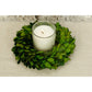 Candle in a glass holder inside a green leaf wreath on a beige surface