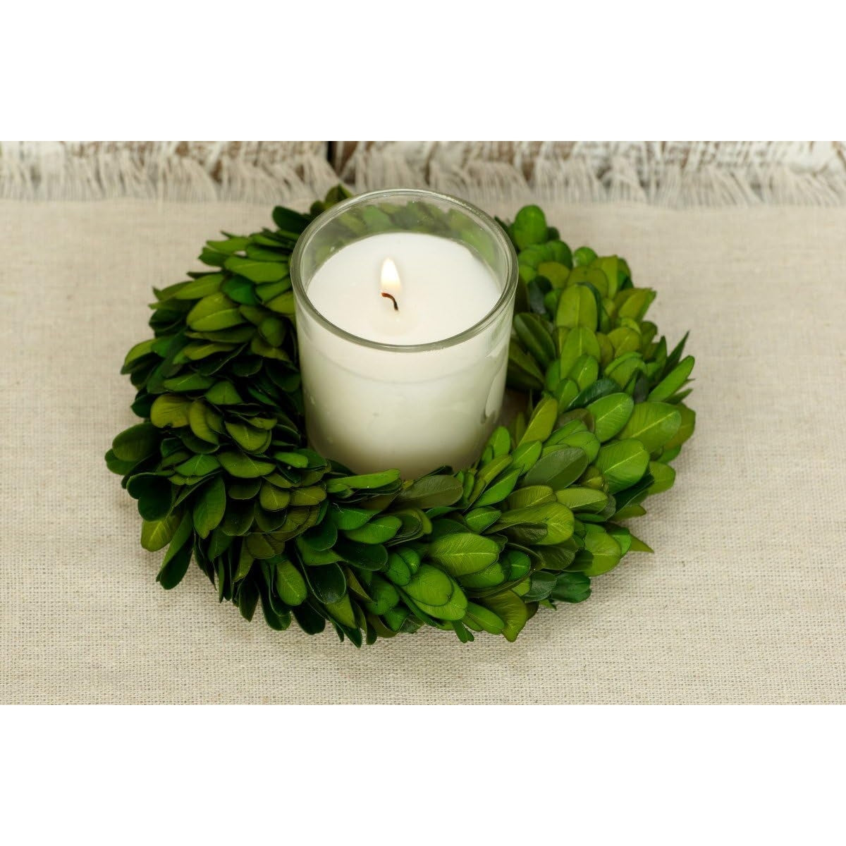Candle in a glass holder inside a green leaf wreath on a beige surface