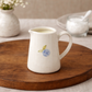 White ceramic pitcher with floral design on a wooden surface