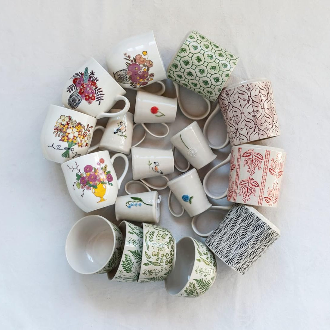 White ceramic pitchers with floral design and bird designs mixed in with a collection of colorful bowls and mugs