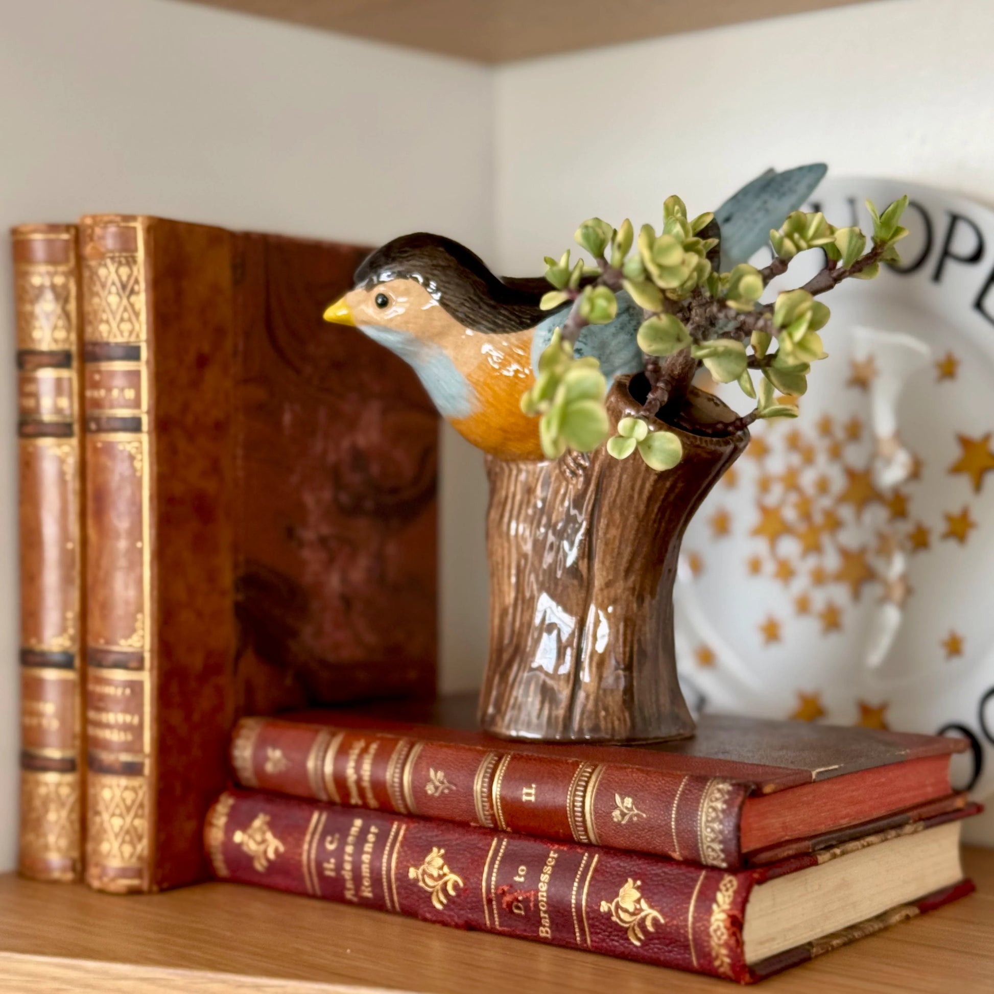 Decorative bird figurine on a stack of books with a vase in the background