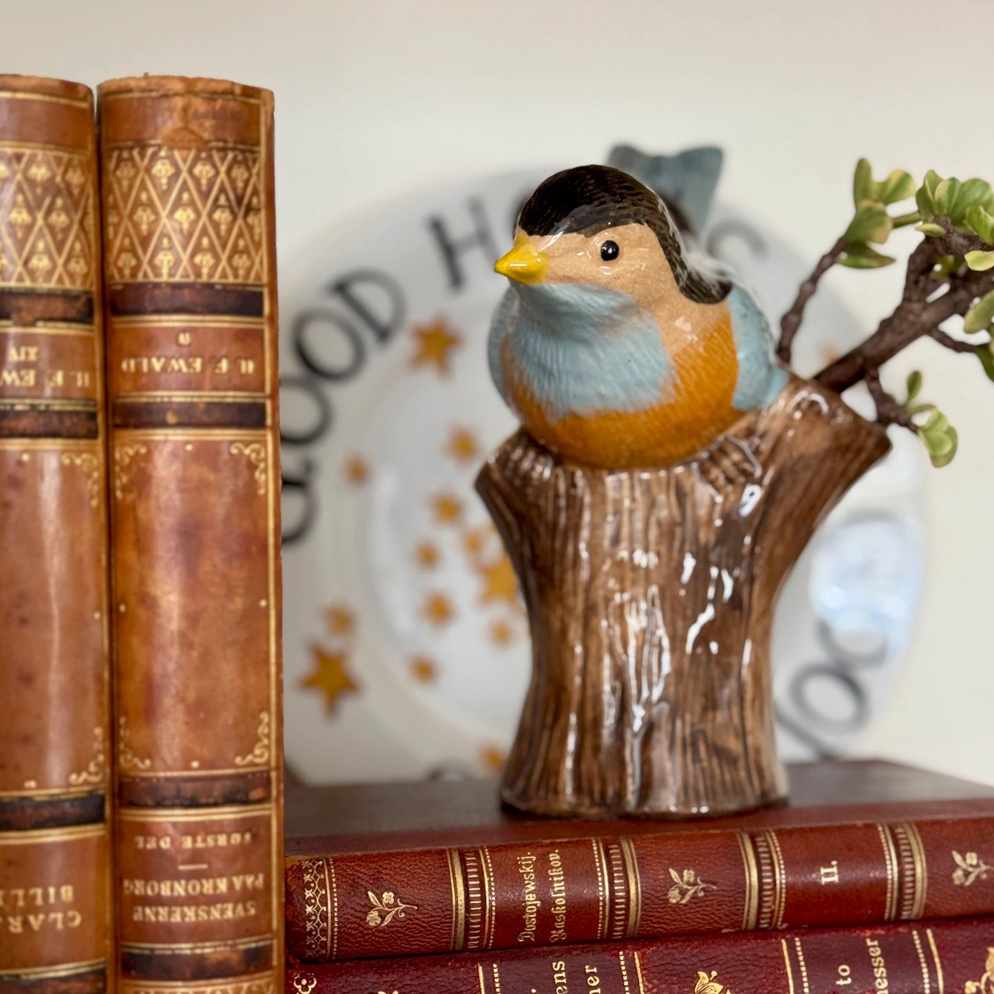 Decorative bird figurine on a branch with vintage books and a blurred background