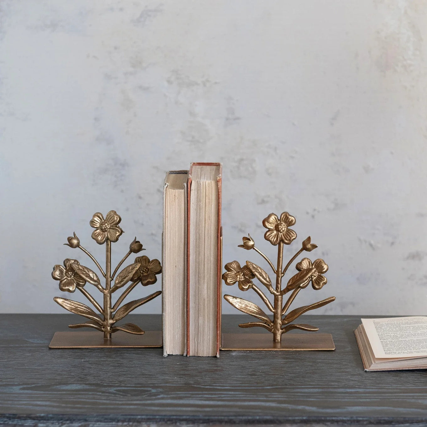 A pair of gold finish cast metal flower bookends with intricate floral designs on a square base.