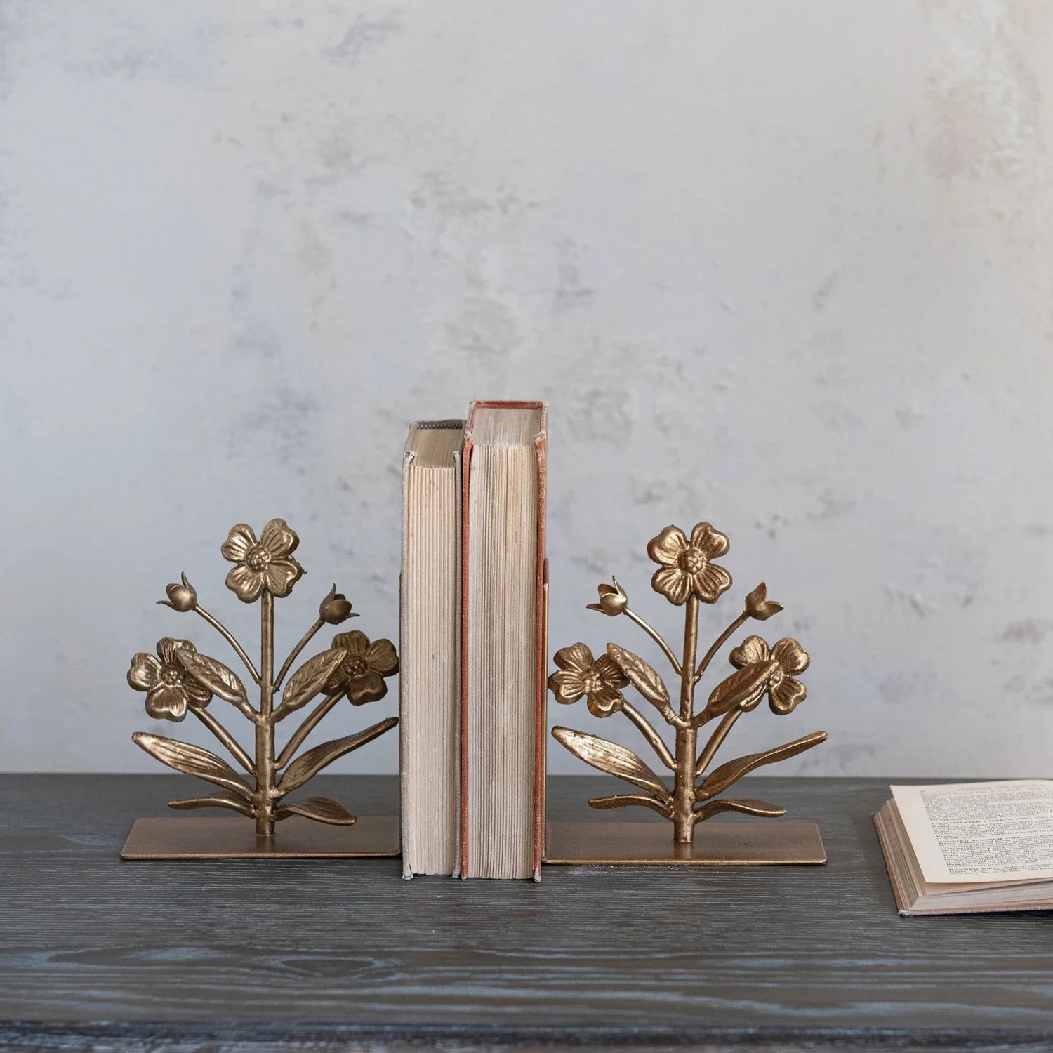 A pair of gold finish cast metal flower bookends with intricate floral designs on a square base.