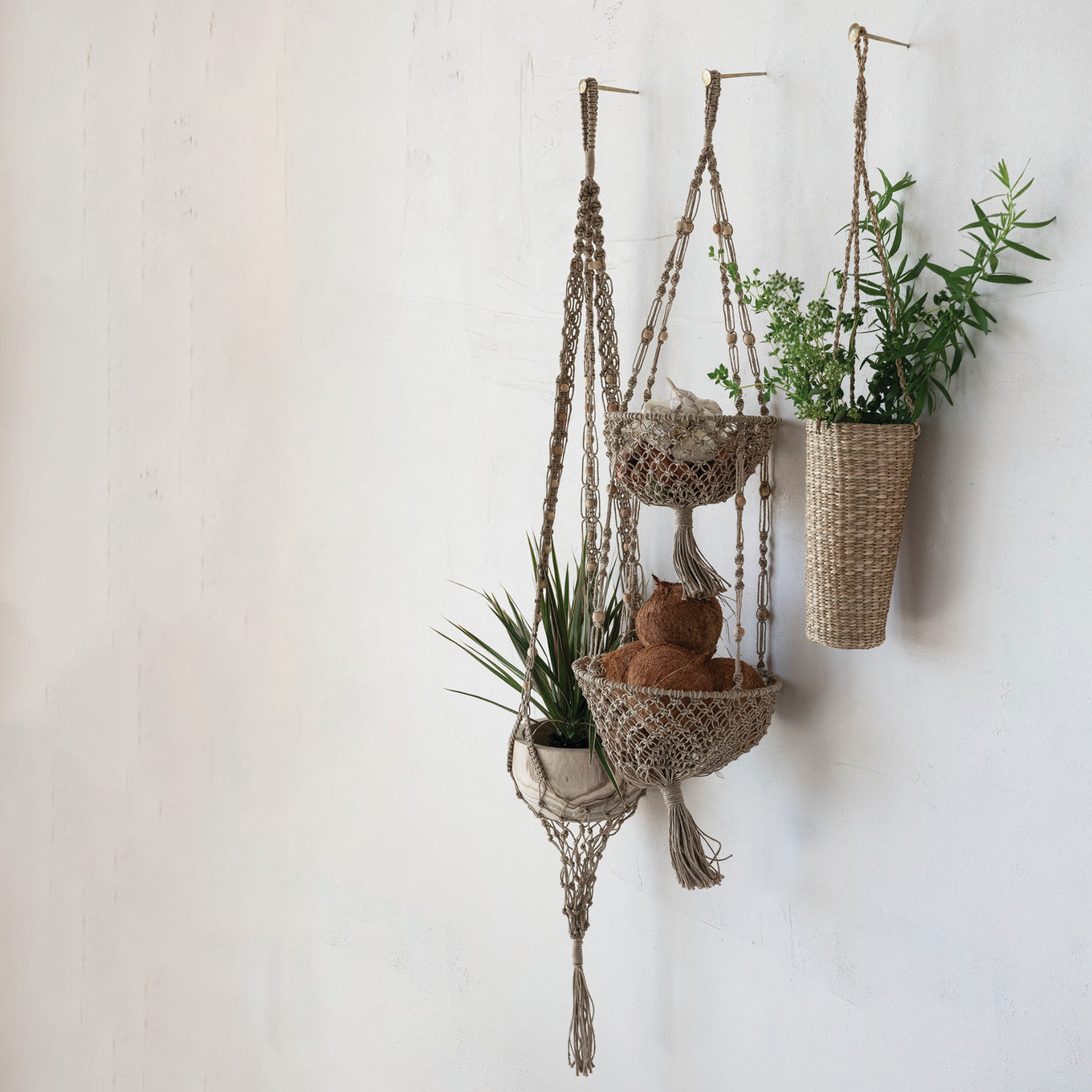 Macrame plant hanger with multiple plant pots against a white wall