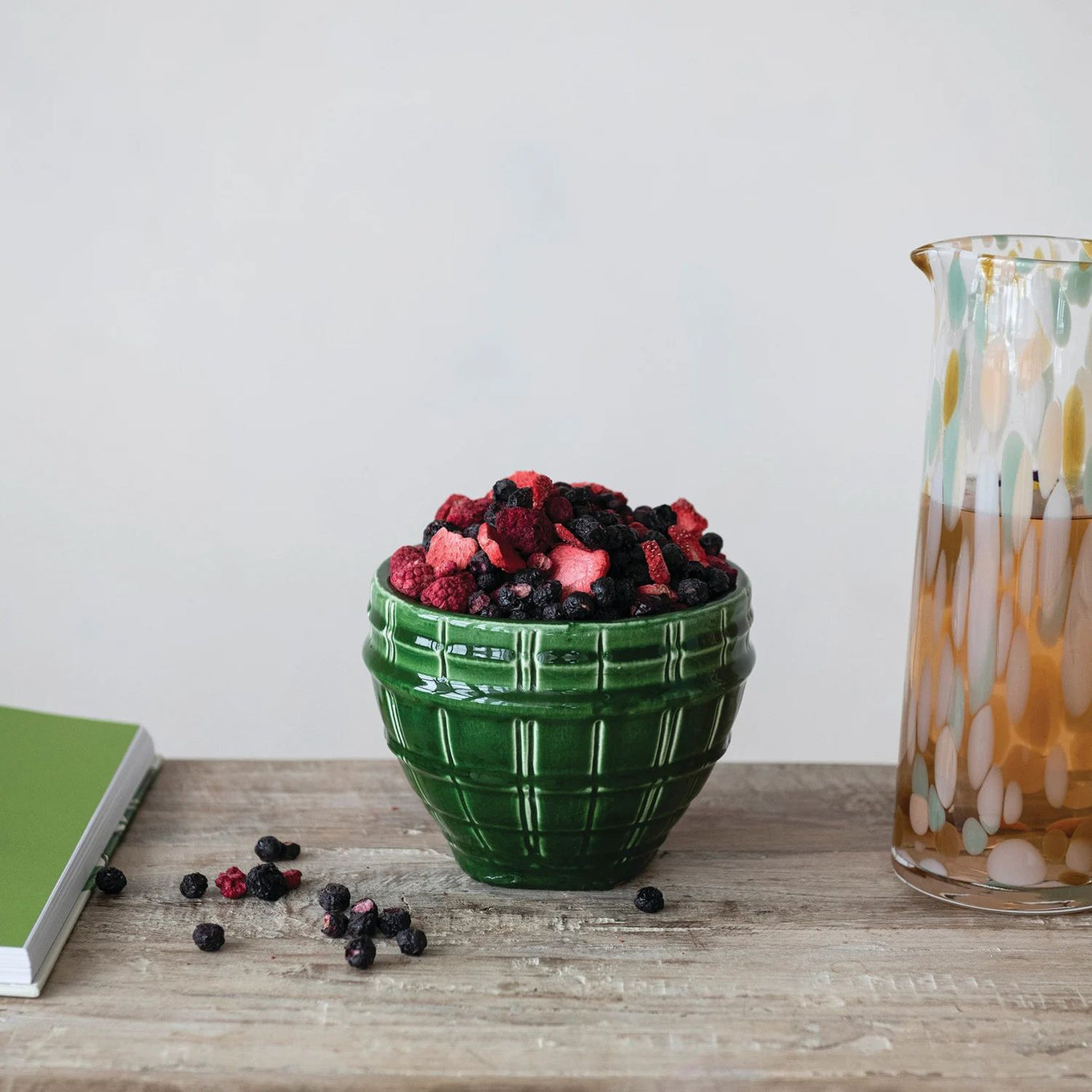 Green bowl filled with berries on a wooden surface next to a glass container.