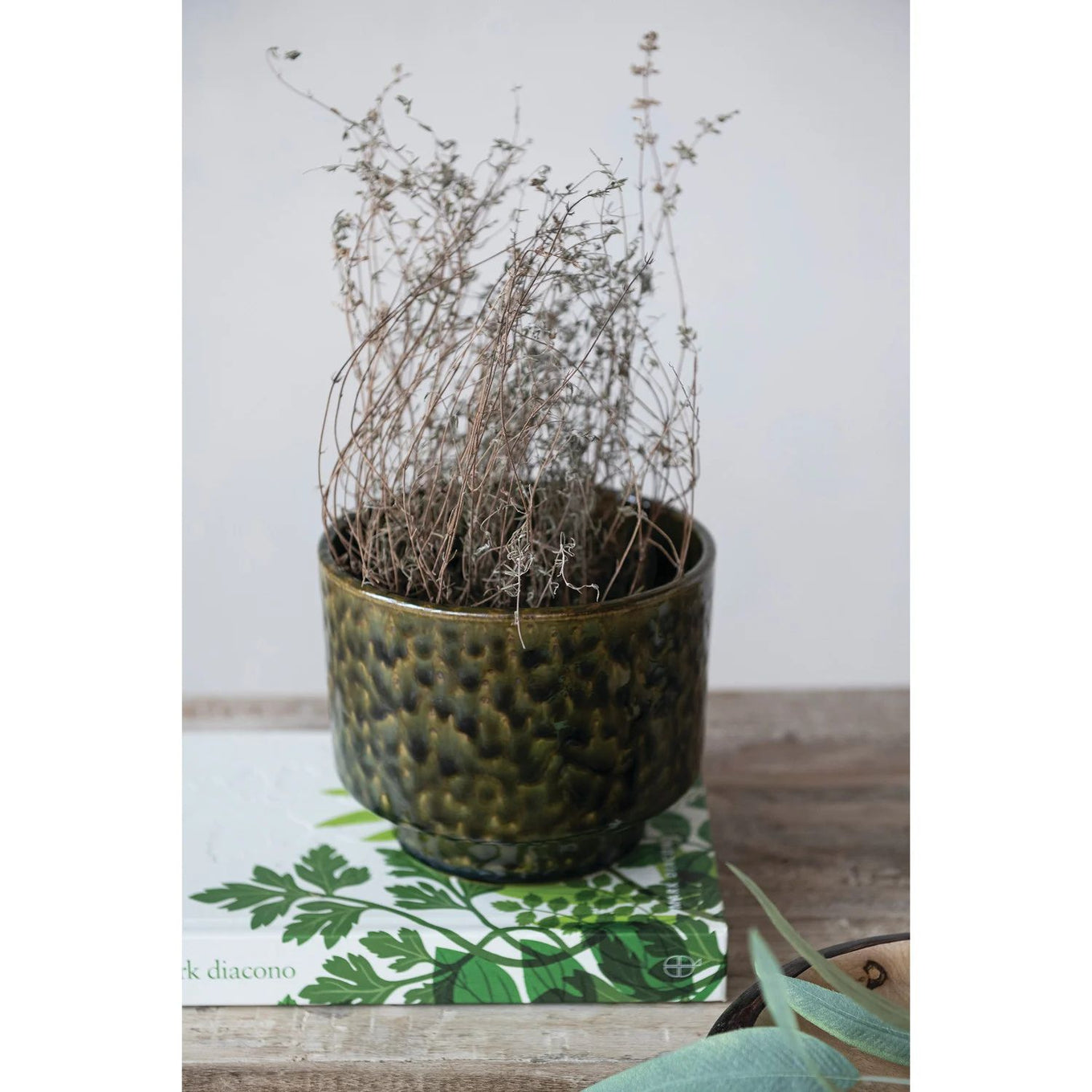 Decorative pot with dried plants on a wooden surface