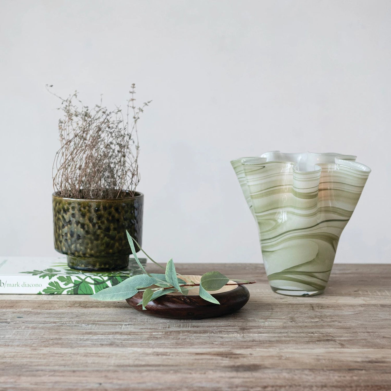 Decorative vase with wavy pattern on a wooden surface with a plant and book in the background.