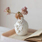 White decorative vase with floral designs on a surface with an open book