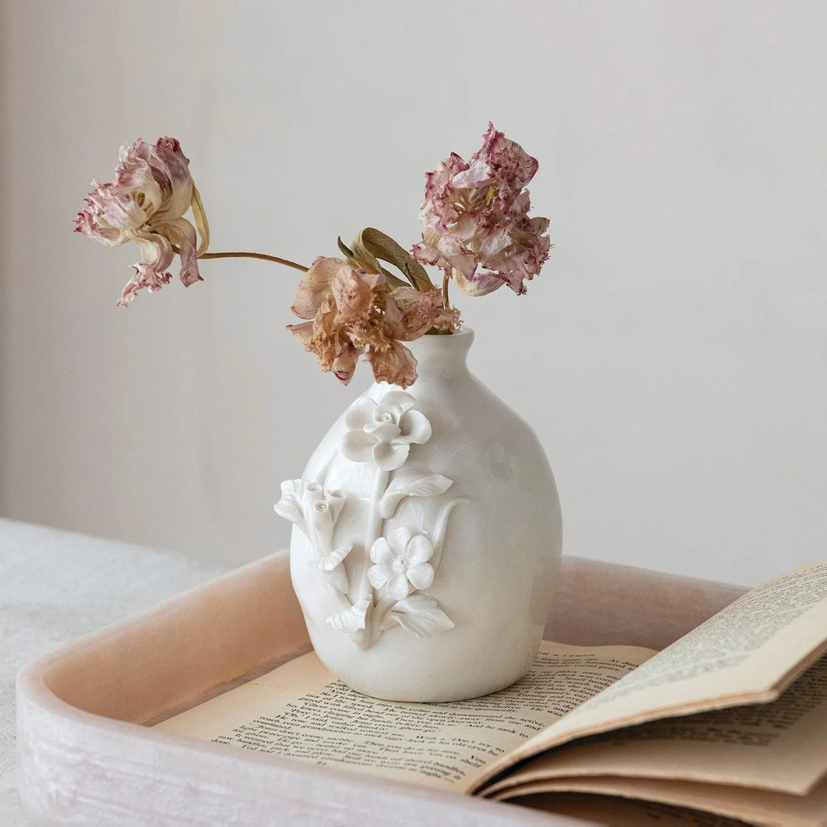 White decorative vase with floral designs on a surface with an open book