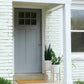 Gray front door of a house with plants and a doormat on a white brick wall.