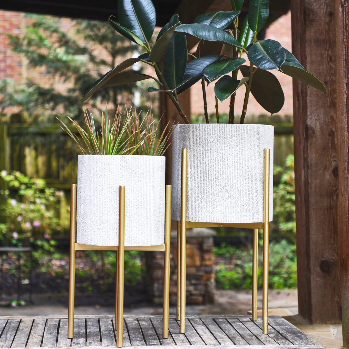 Two decorative planters with gold stands on a wooden deck with plants.