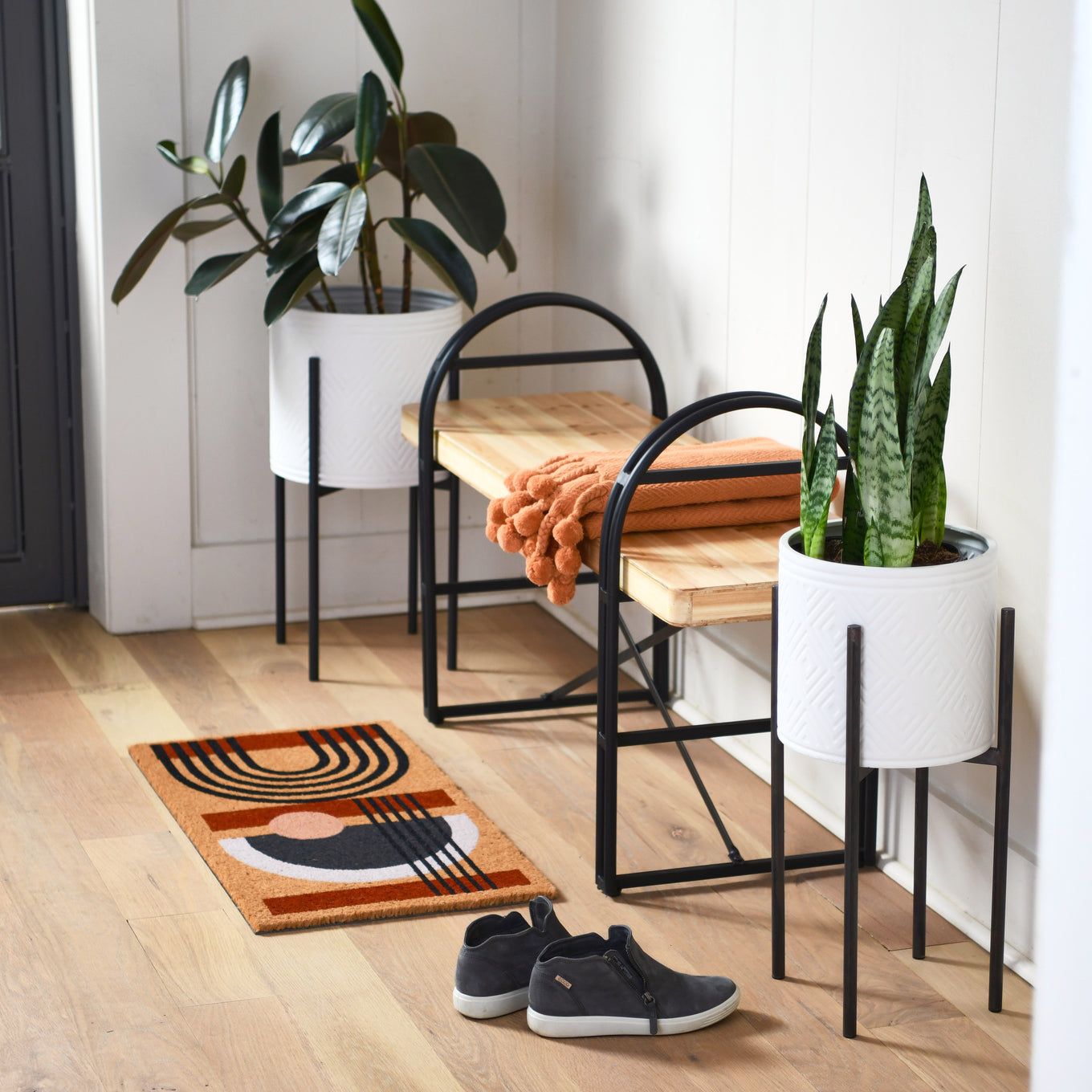 Modern interior with wooden bench, planters, and a doormat on a wooden floor.