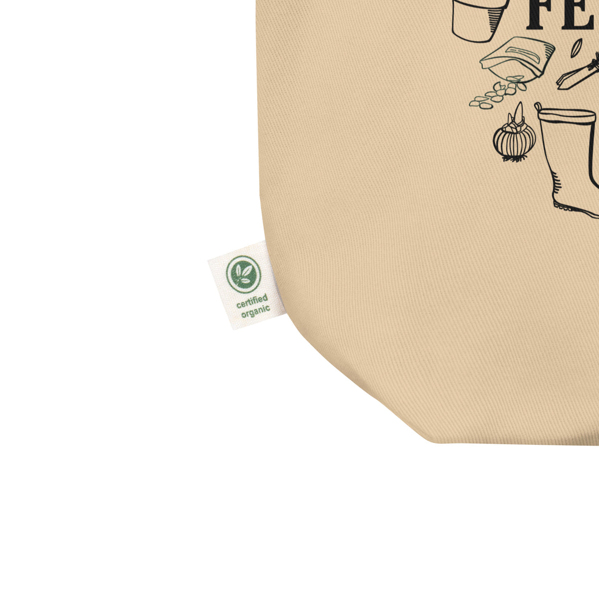 Close-up of a beige canvas tote bag corner with black print and a small white 'certified organic' tag attached near the edge, shown on a white background.