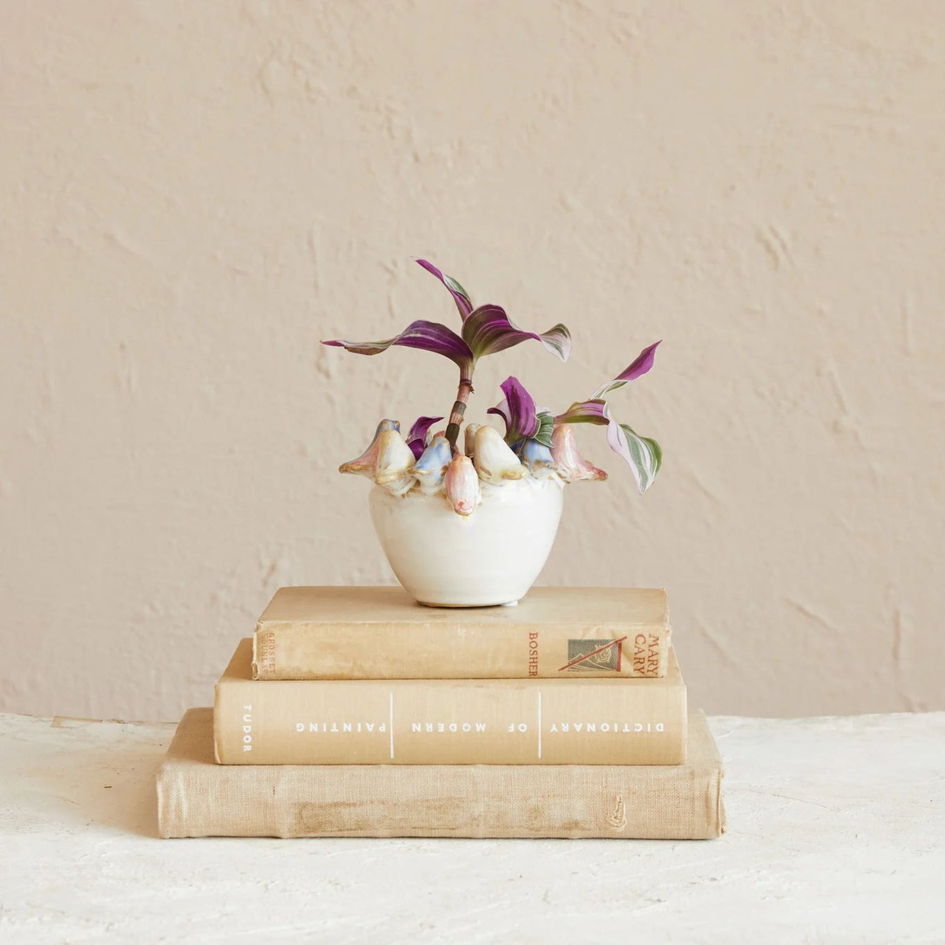 Small white vase with decorative birds and flowers on top of vintage books against a beige background