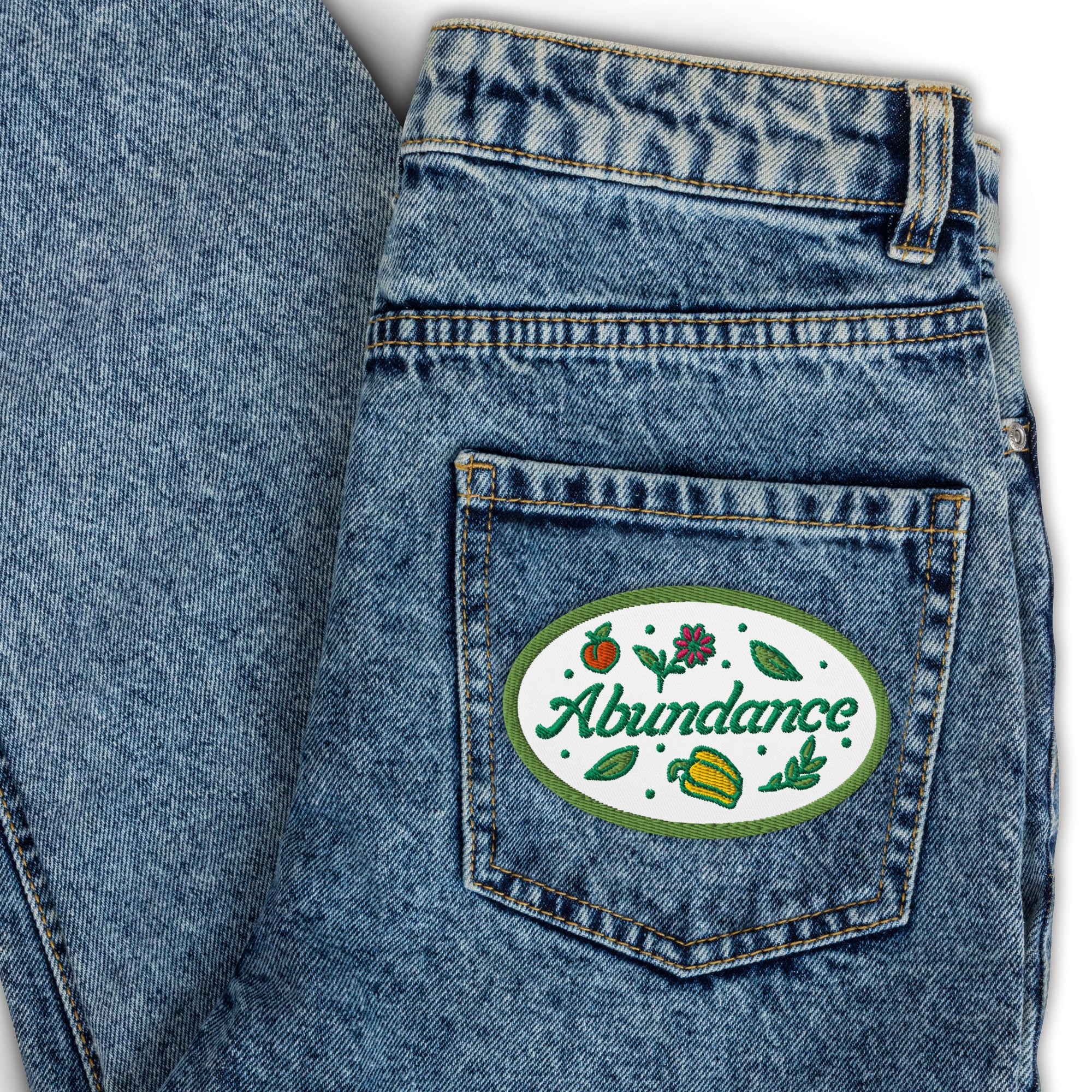 Denim pocket with 'Abundance' patch featuring fruits and leaves.