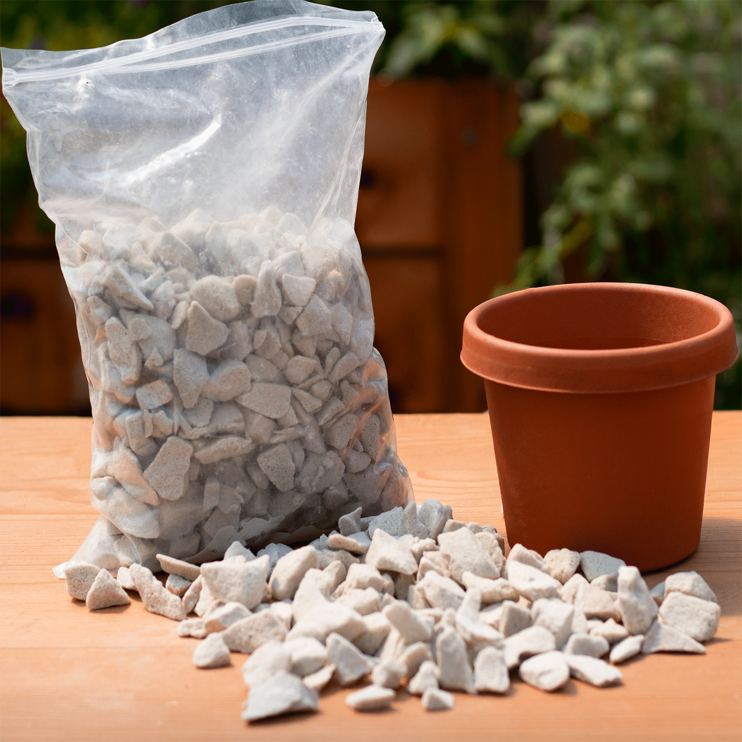 An image of the soilless growing media sitting in the bag it is manufactured and sold in. These stones are splayed out in front of a reddish-orange pot for reference. Pot is small. POT IS NOT INCLUDED.